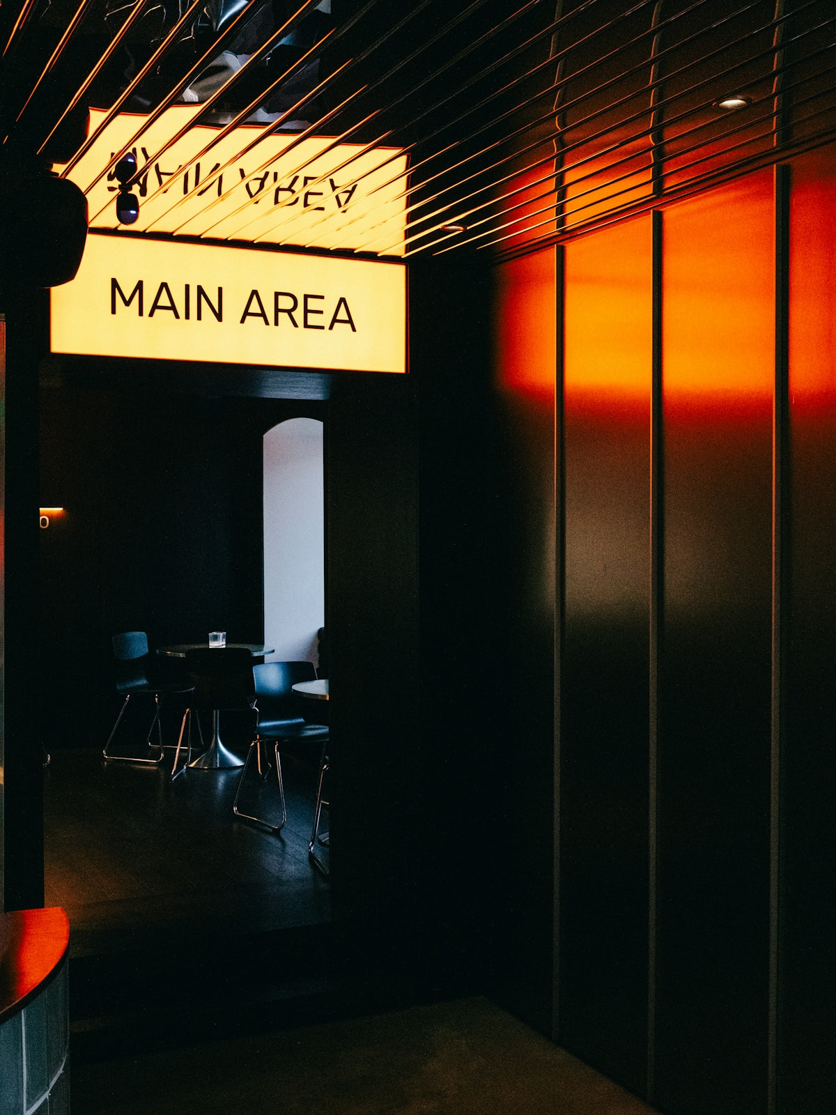 Illuminated sign points towards a dimly lit main area