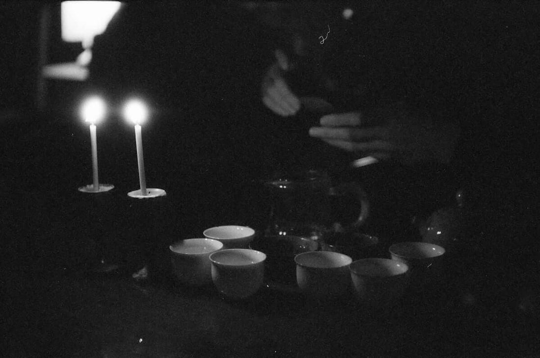 Two candles and tea cups set on a dark table, creating a tranquil atmosphere for enjoying a lavender serenity candle.