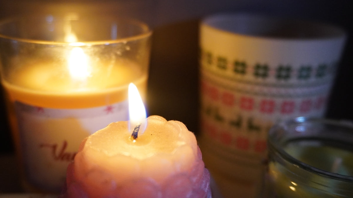 Two lit candles with a decorative mug behind.