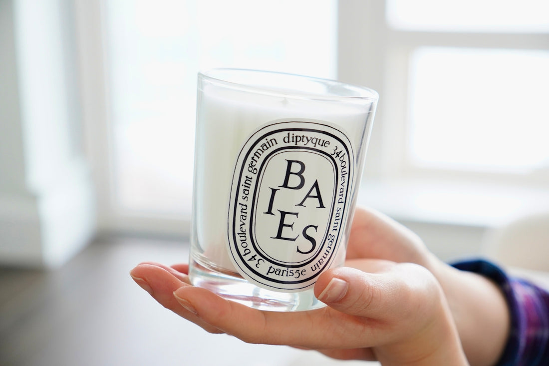 Hands holding a scented candle in a glass jar.