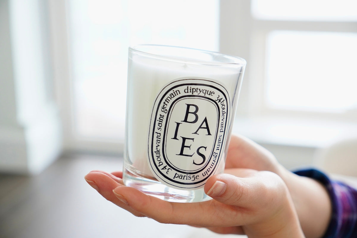 Hands holding a scented candle in a glass jar.