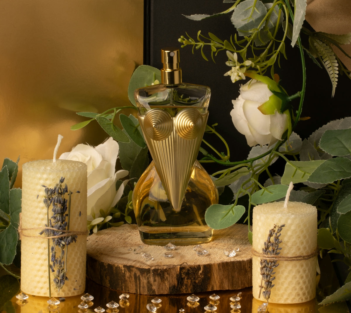 Perfume bottle, two candles, and flowers on a wood base.