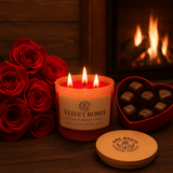 Velvet Roses Soy Candle with roses and chocolates beside a warm fireplace, creating a romantic ambiance.